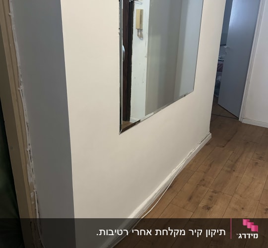 קיר פנימי צבוע בלבן עם מראה מותקנת ורצפת פרקט בדירה